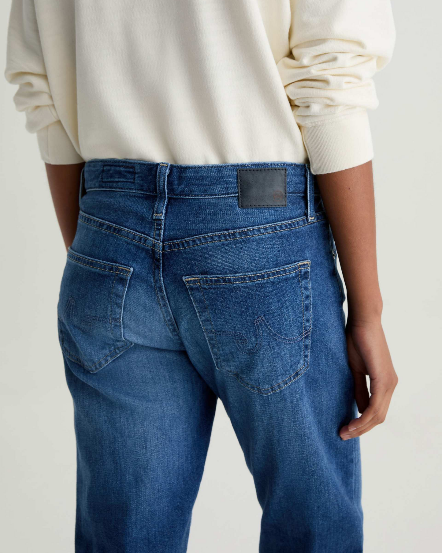 Person wearing blue jeans with a visible brand label on a light gray background