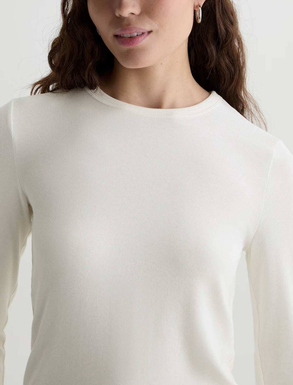 A close-up of a woman wearing a ribbed, long-sleeve crewneck top in off-white or cream.