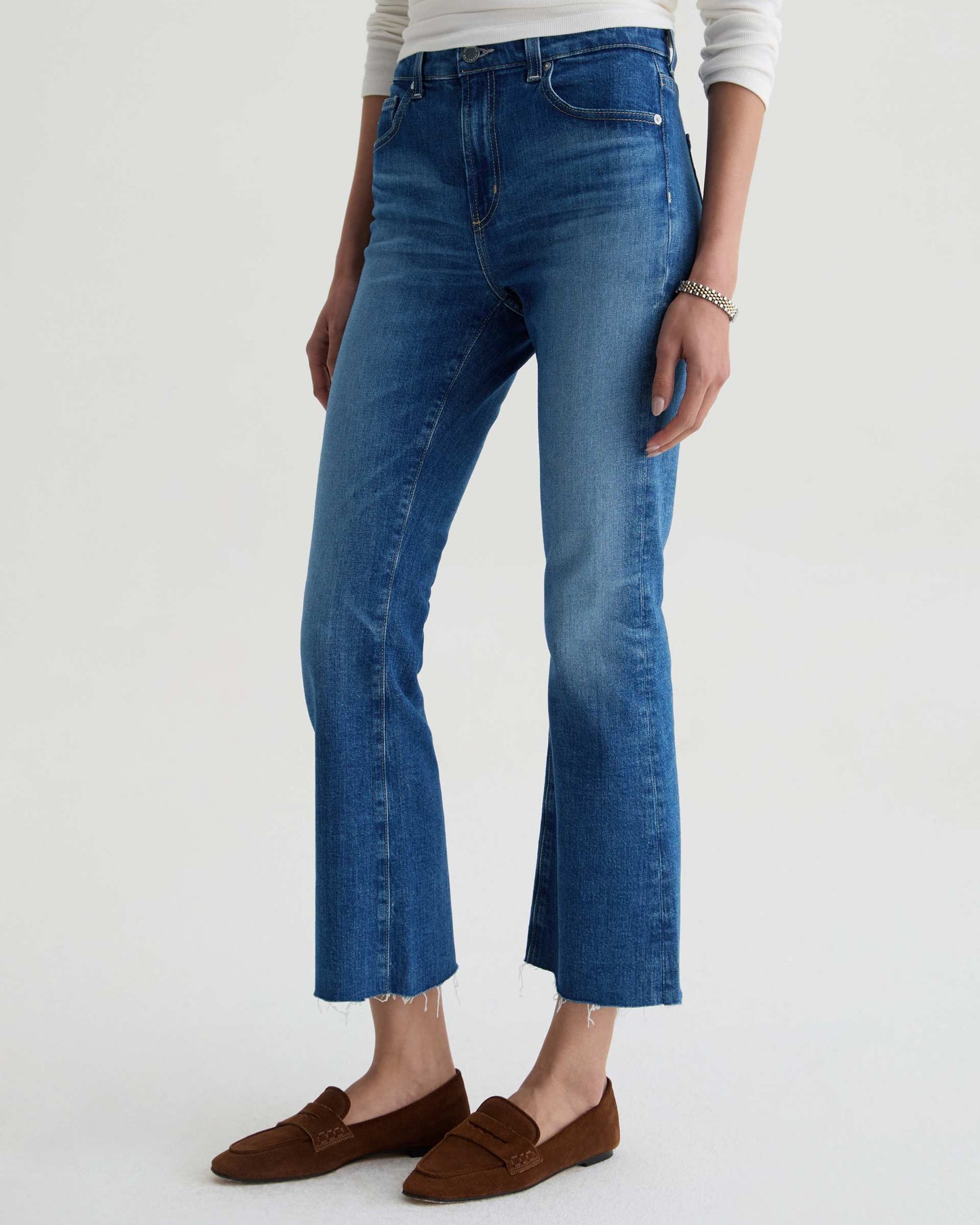 Person wearing blue jeans and brown loafers on a white background