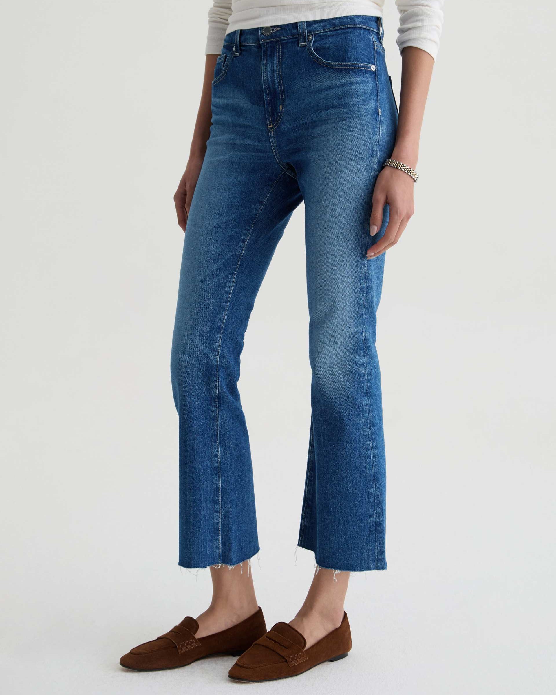 Person wearing blue jeans and brown loafers on a white background