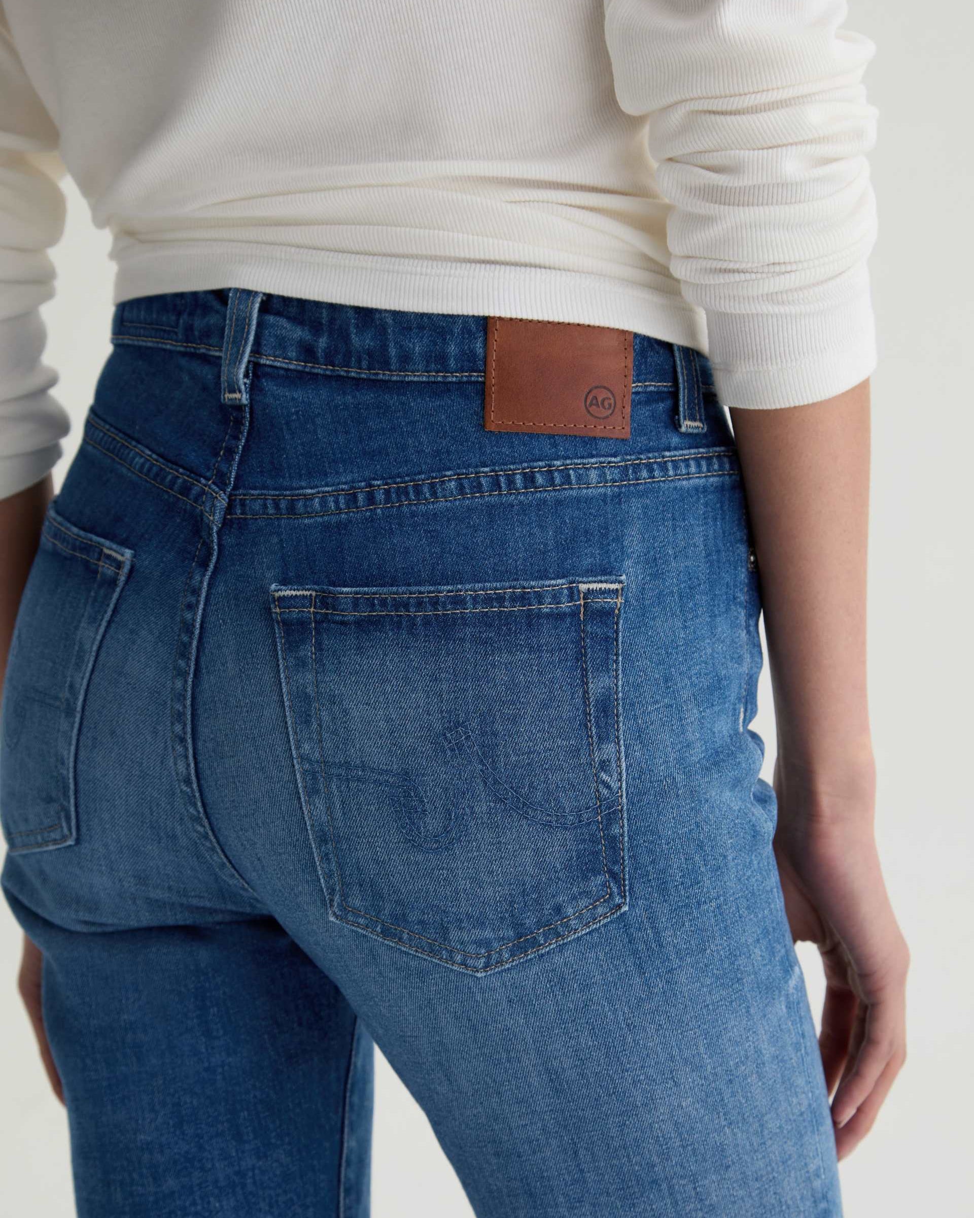 Person wearing blue jeans with a visible brand label on a plain background
