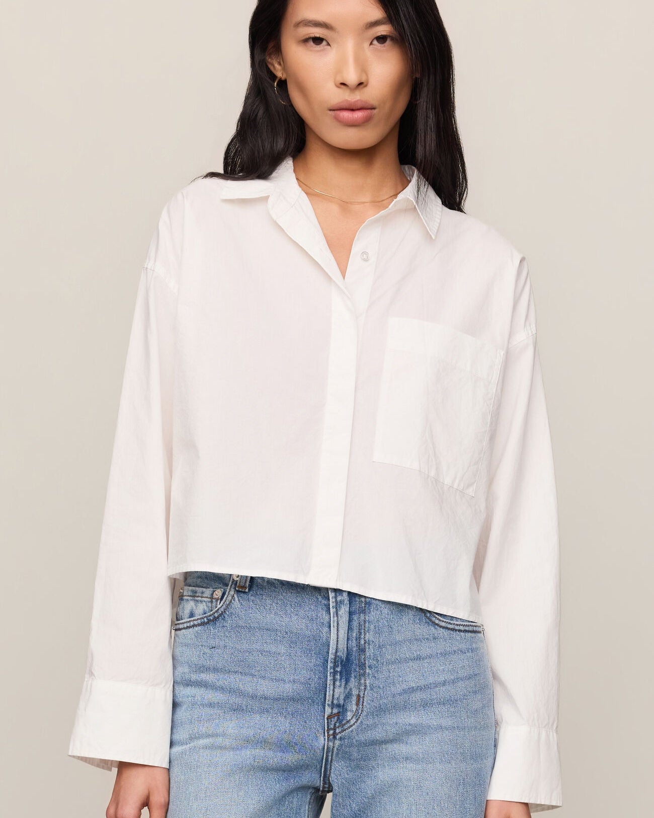 Woman wearing a white shirt and blue jeans against a plain background