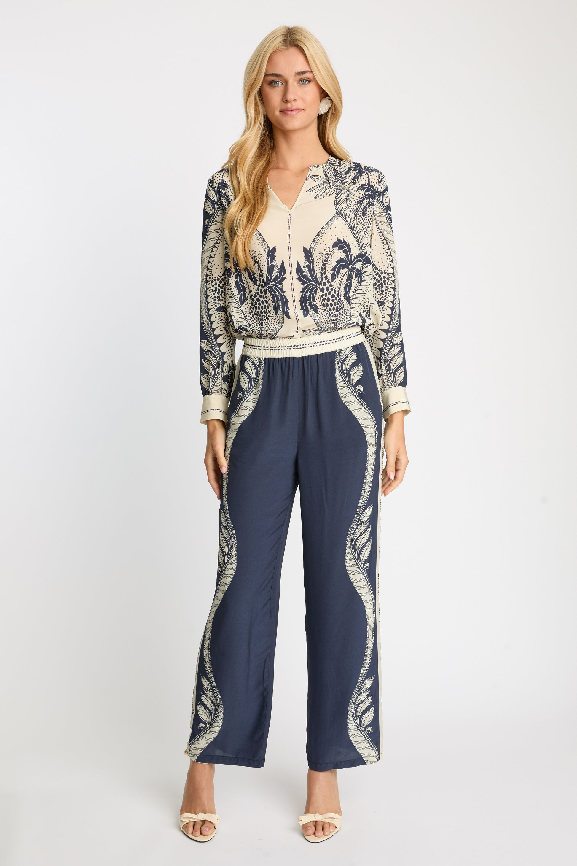Woman wearing a patterned top and navy pants on a white background