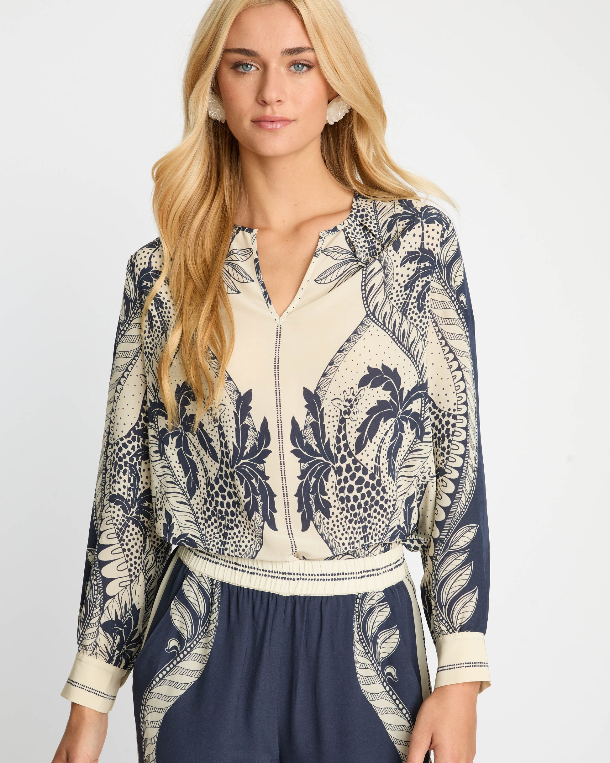 Woman wearing a blue and white patterned blouse with navy pants on a white background