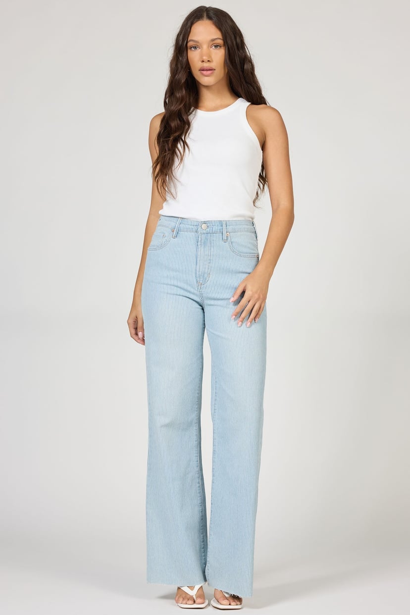 Woman wearing light blue jeans and a white top on a plain background