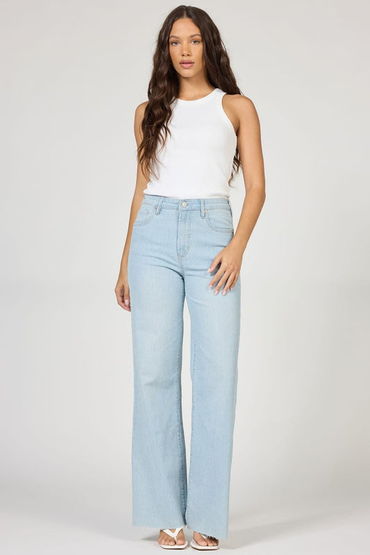 Woman wearing light blue jeans and a white top on a plain background