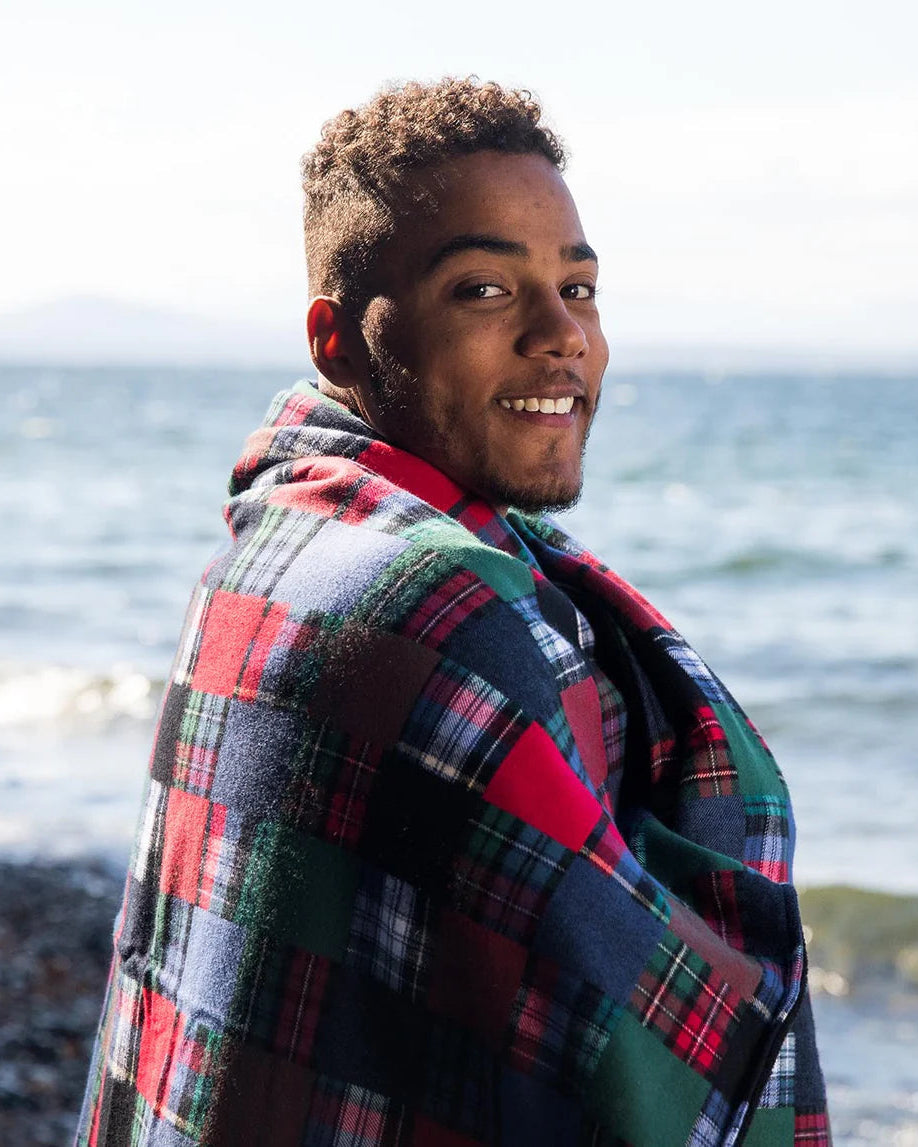 Man wearing a plaid blanket over his shoulders by the ocean