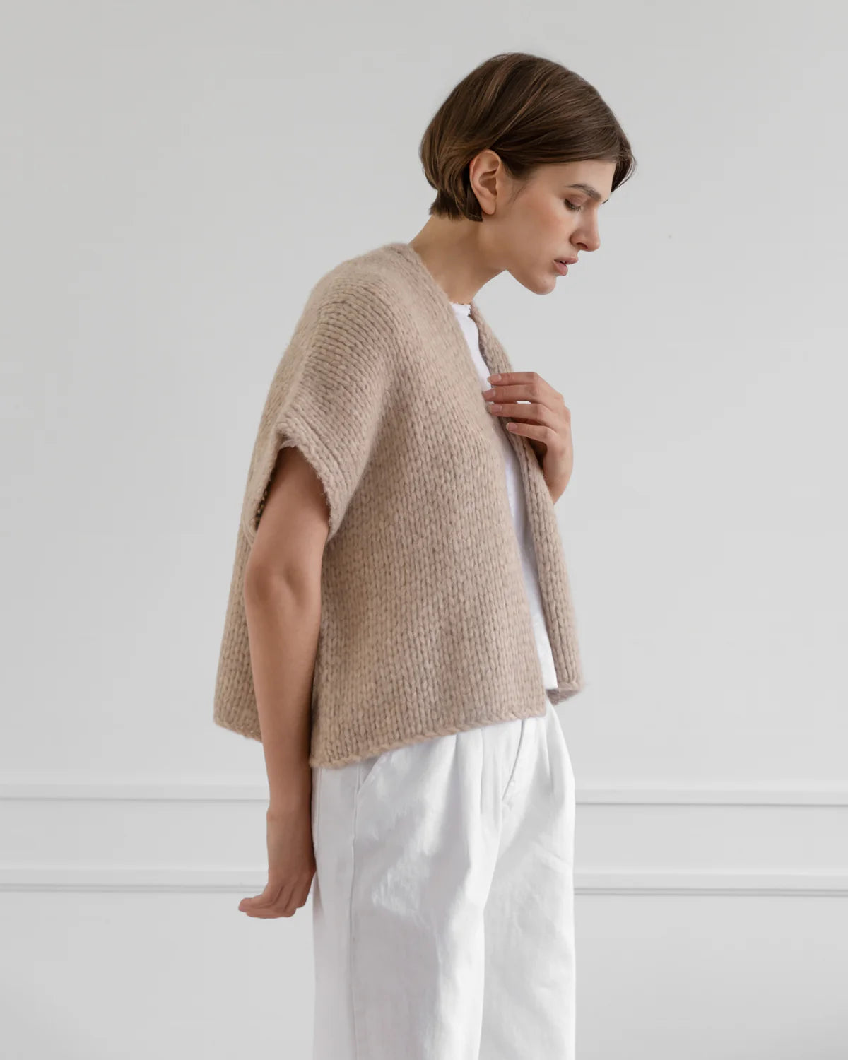 Woman wearing a beige knitted poncho against a white background