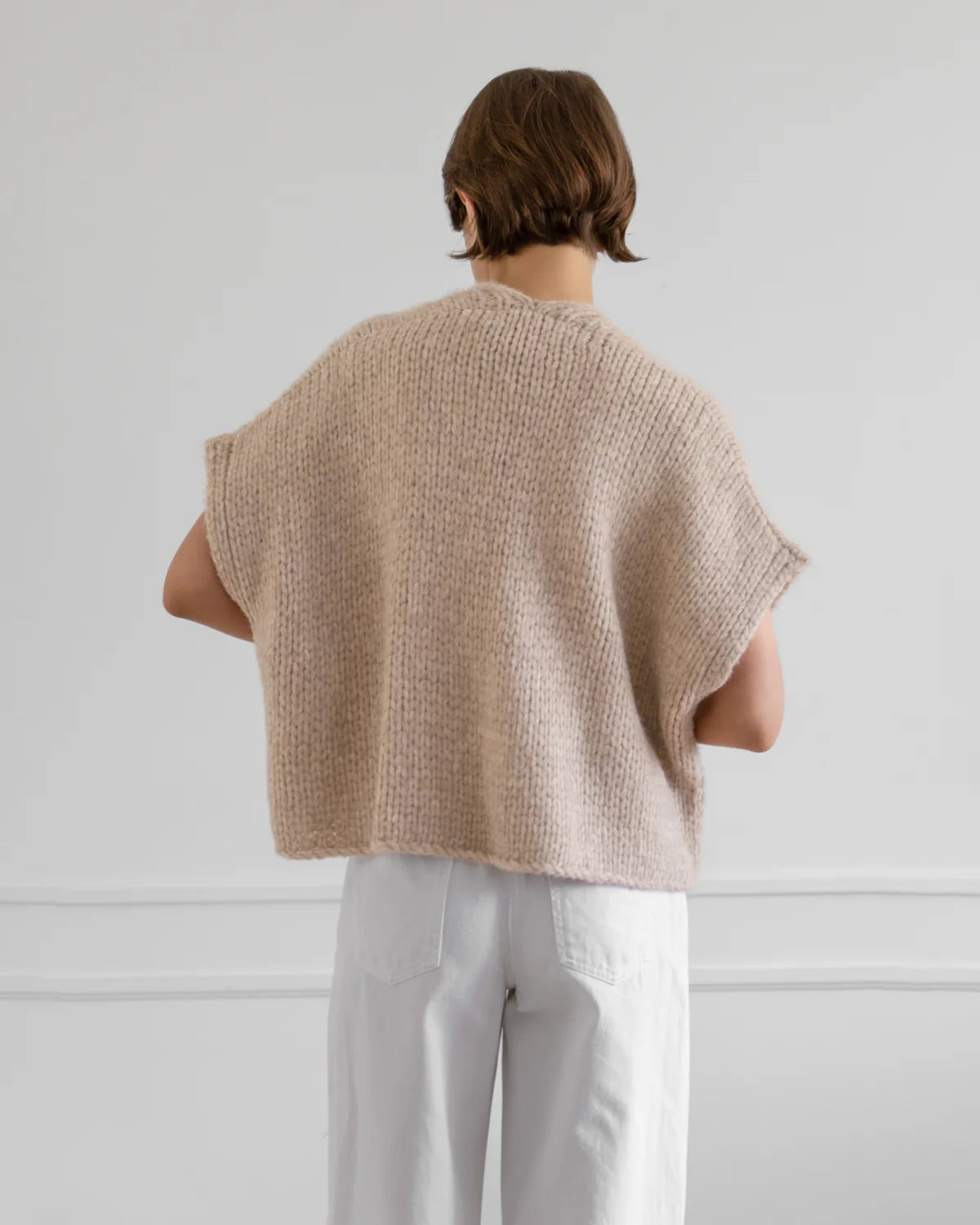 Person wearing a beige knitted vest against a white background