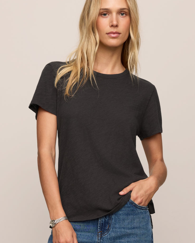 Woman wearing a black t-shirt and blue jeans against a beige background