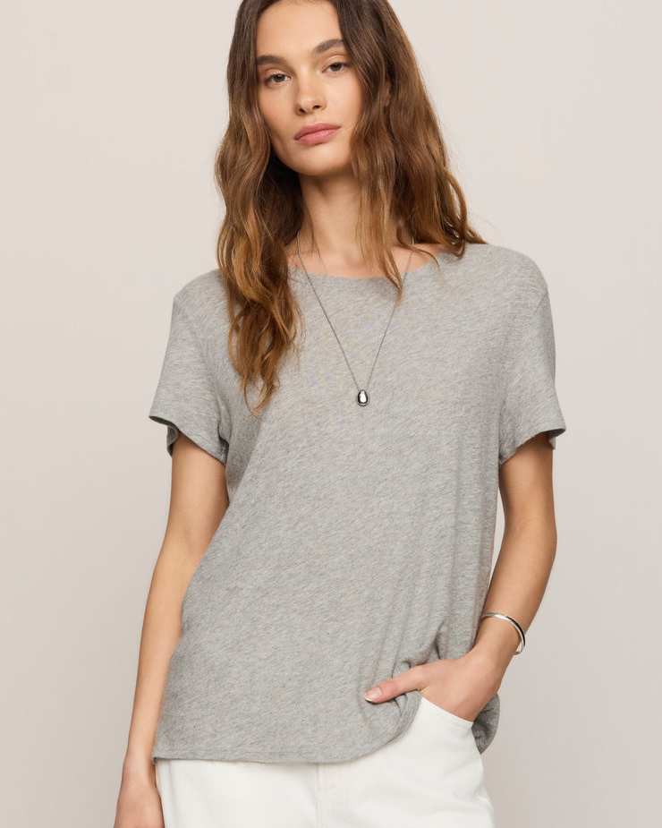 Woman wearing a gray t-shirt and white pants against a plain background