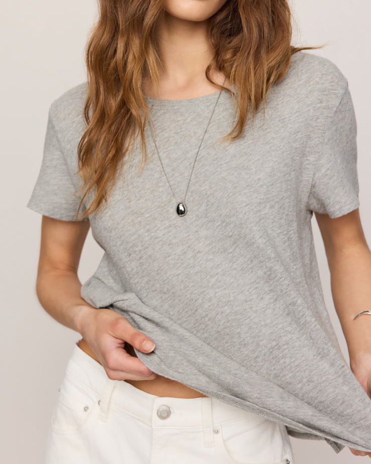 Woman wearing a gray t-shirt and white pants against a plain background