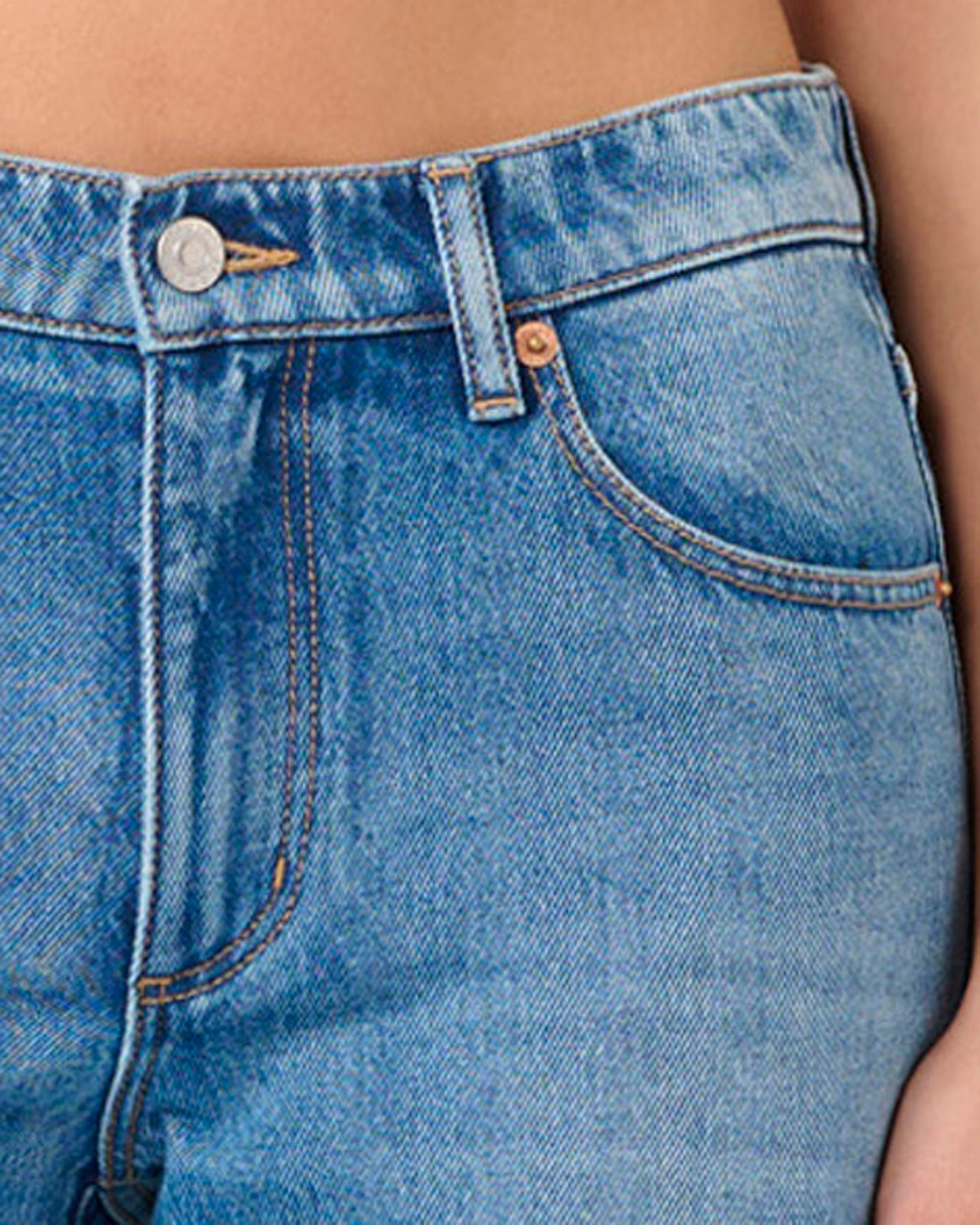 Close-up of blue denim jeans with a focus on the waistband and pocket.