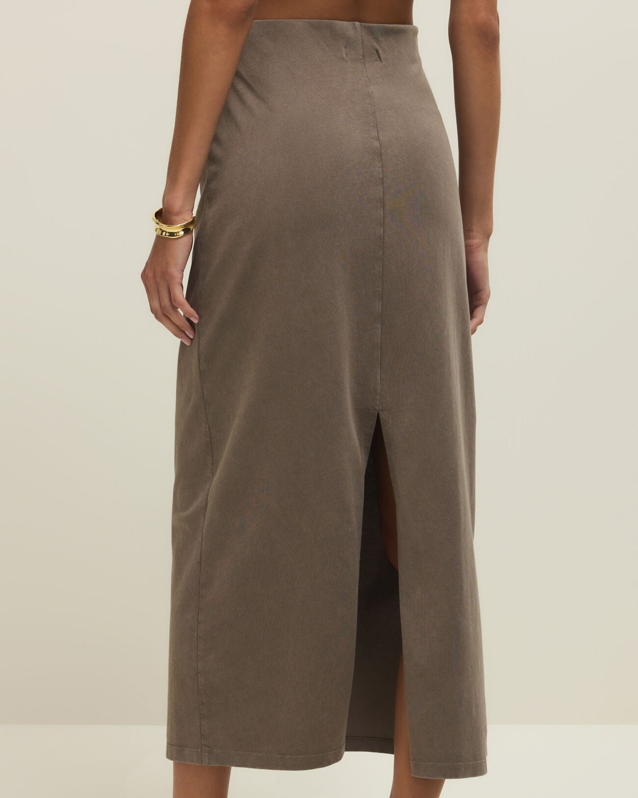 Person wearing a long, light brown skirt on a plain background