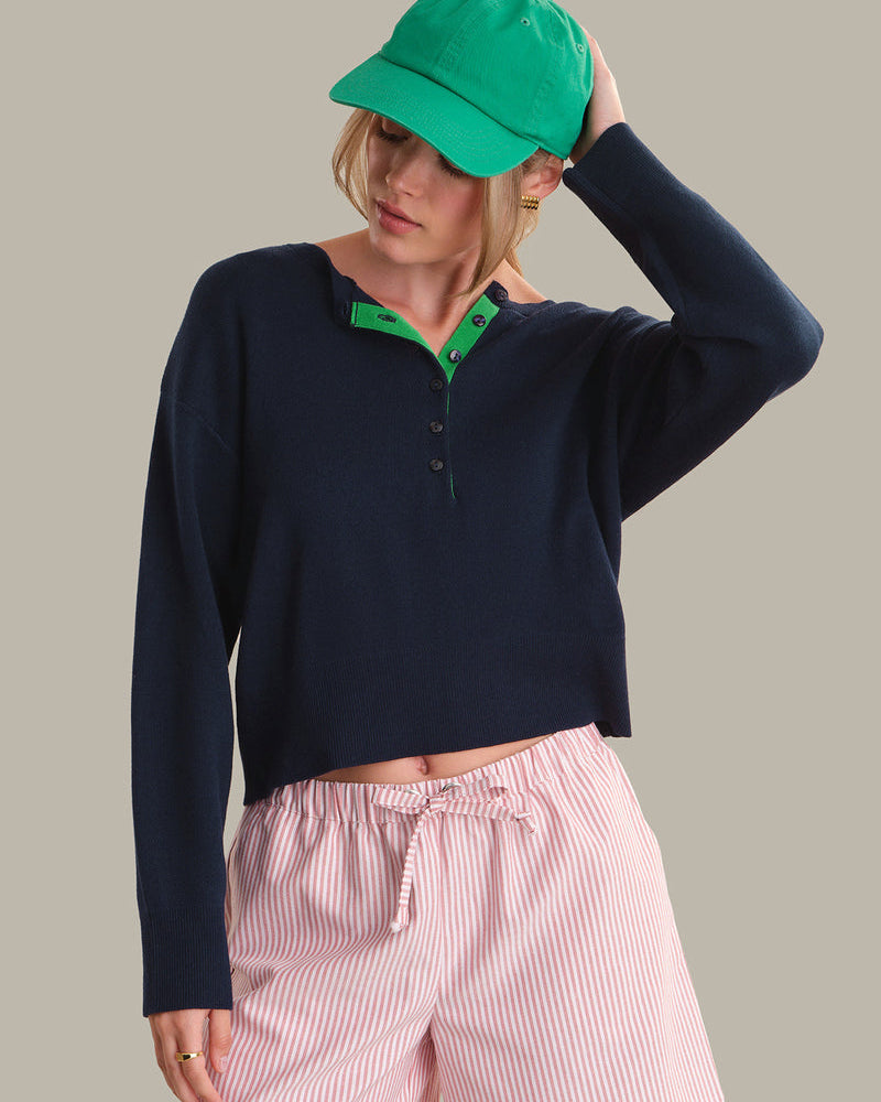 Person wearing a navy long-sleeve shirt with green trim and pink striped pants against a gray background