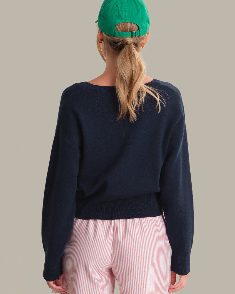 Person wearing a navy blue sweater and pink pants with a green cap on a beige background