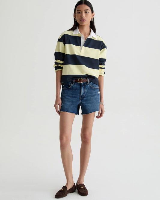 Woman wearing a striped rugby shirt, denim shorts, and brown loafers on a white background