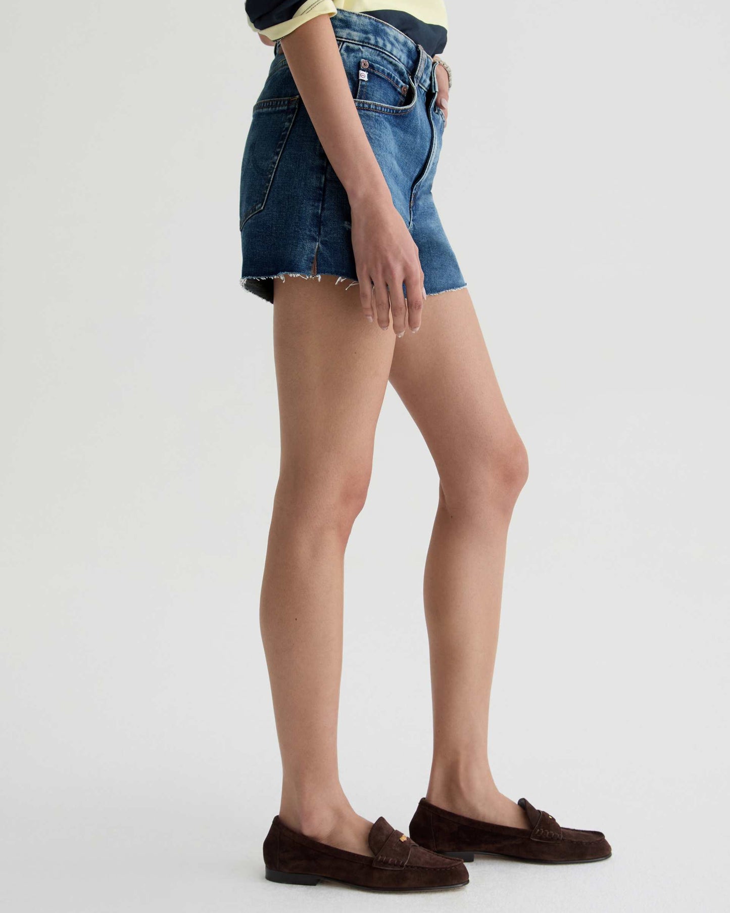 Person wearing blue denim shorts and brown loafers on a white background