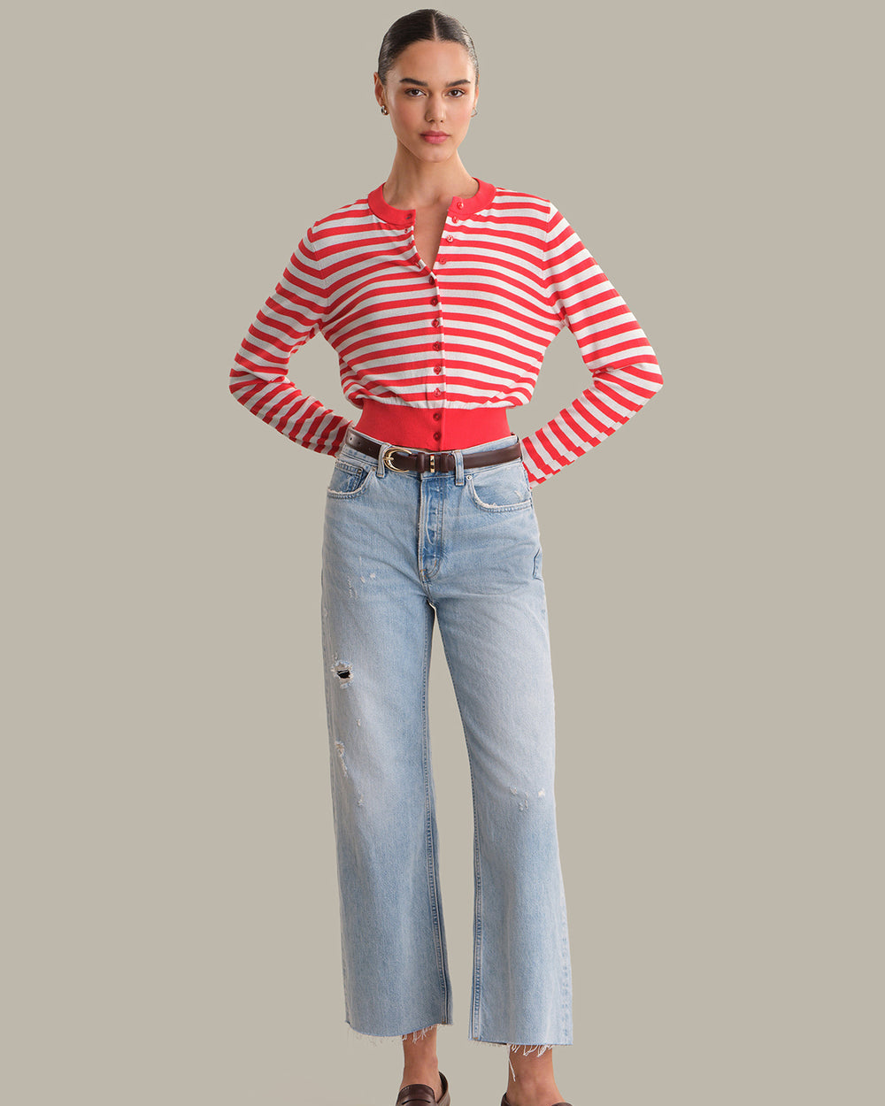 Woman wearing a red and white striped shirt and light blue jeans on a gray background