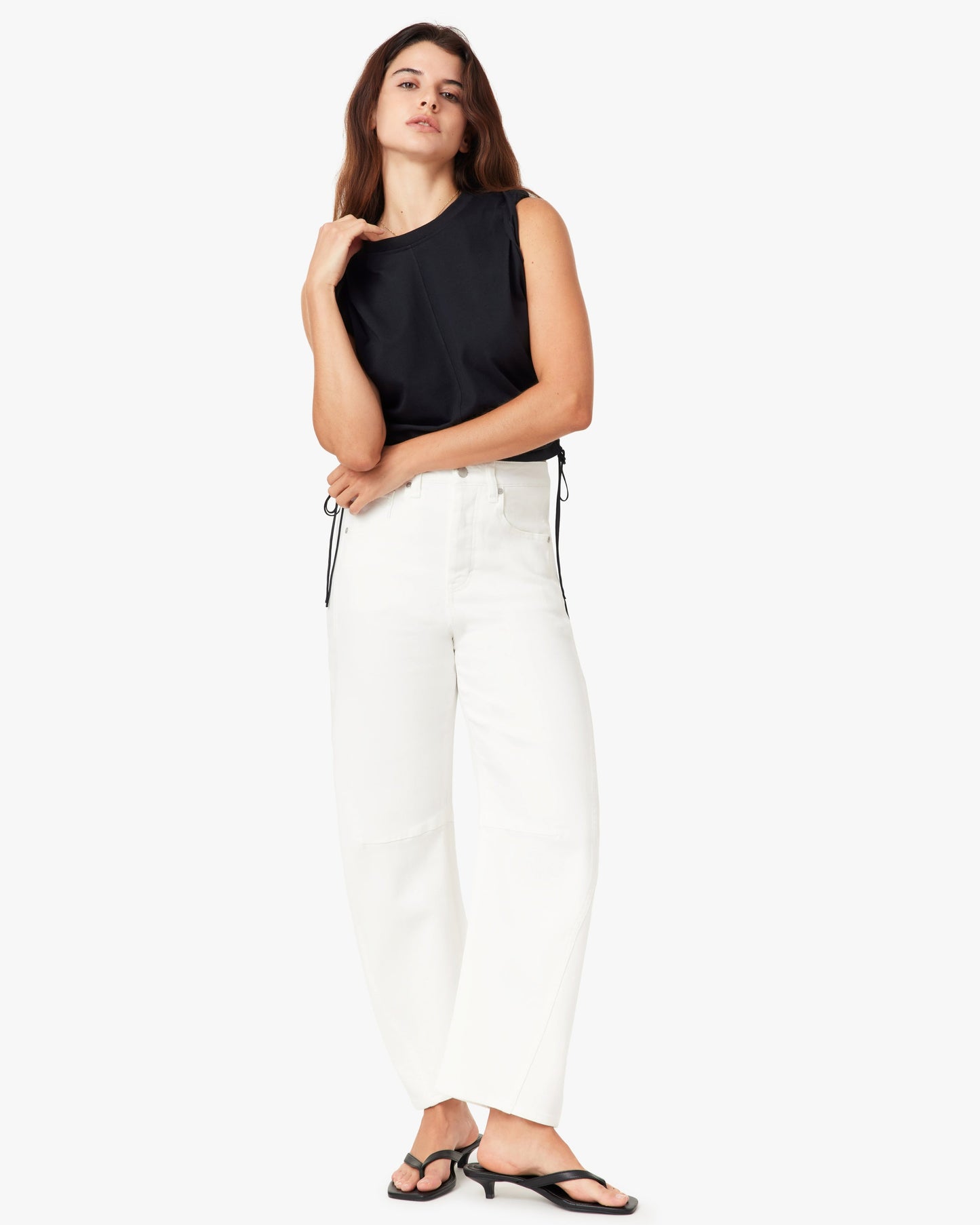 Woman wearing a black sleeveless top and white pants on a white background