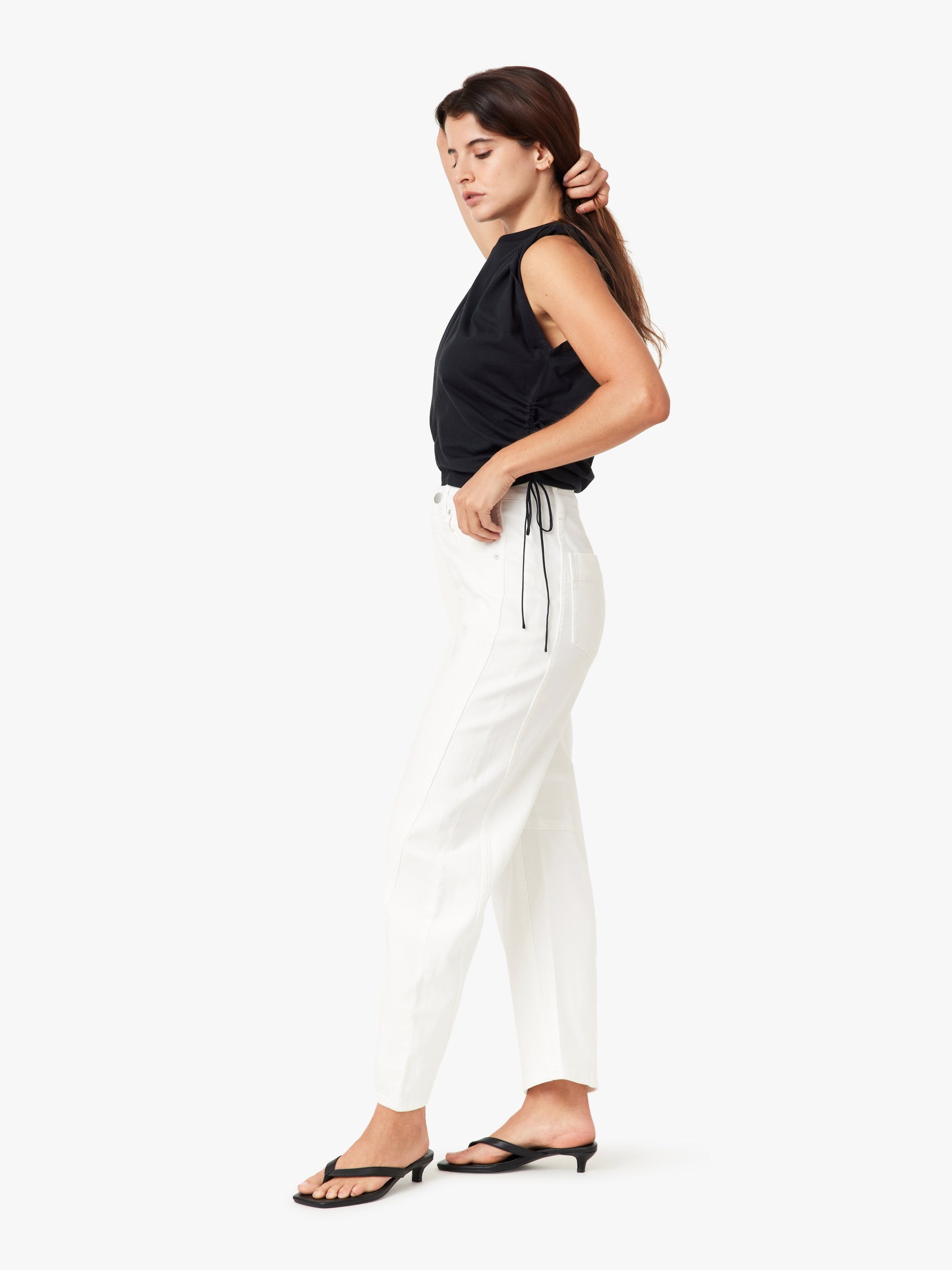 Woman wearing a black sleeveless top and white pants on a white background