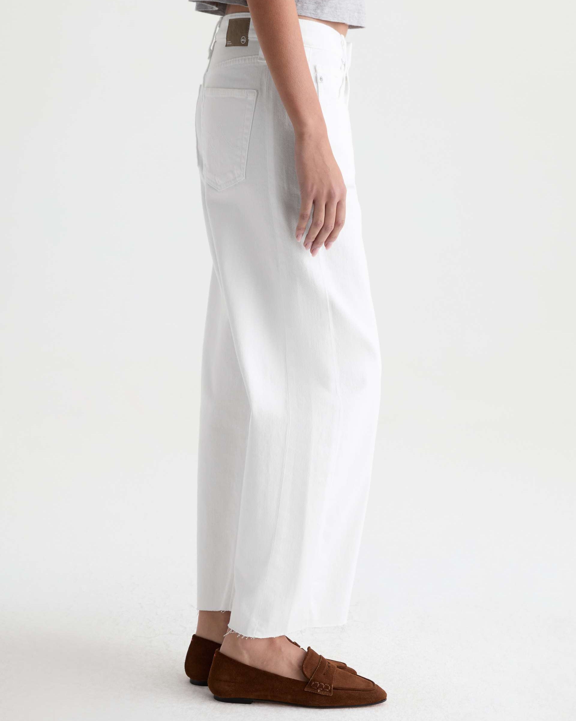 Person wearing white pants and brown loafers on a white background