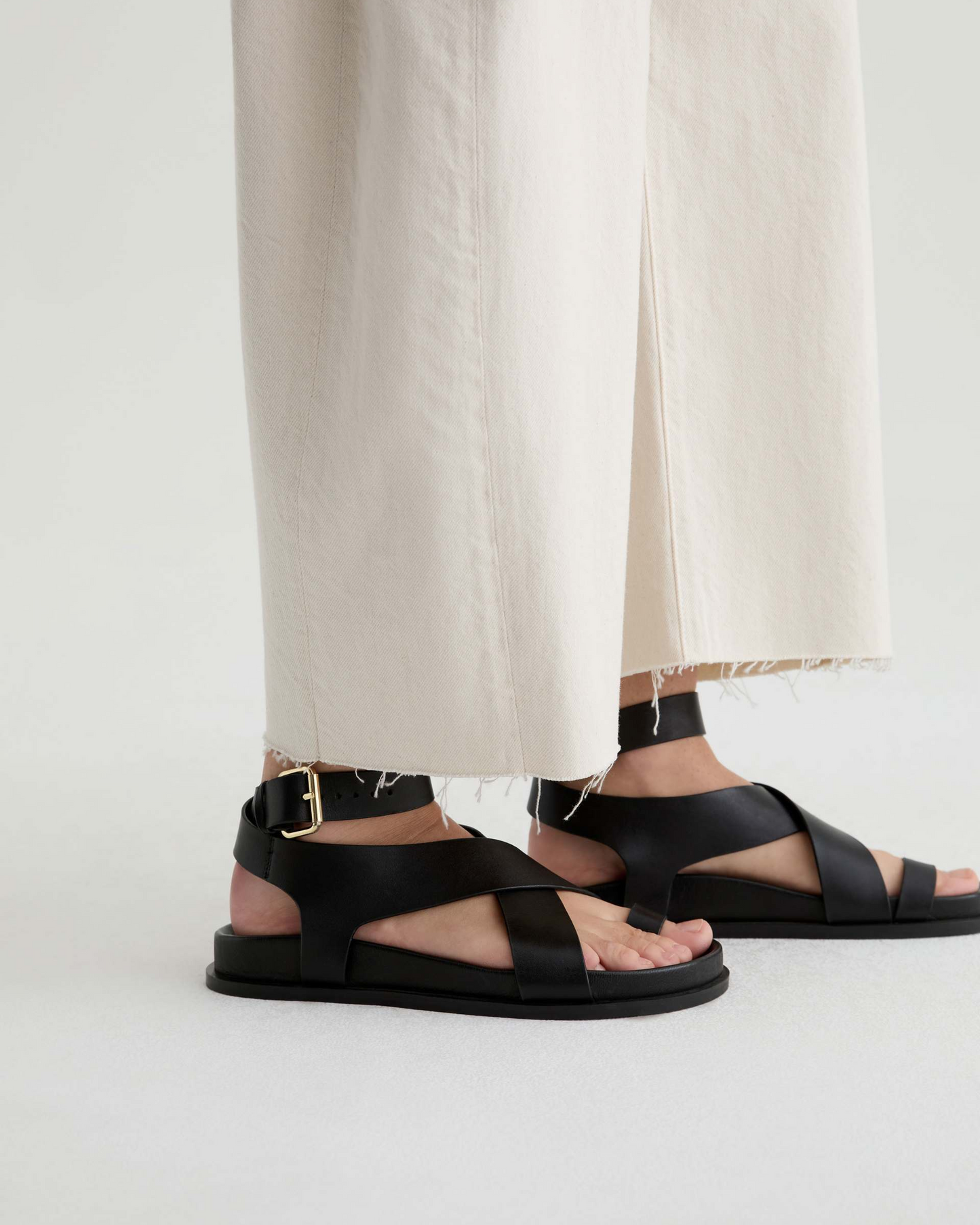 Black sandals worn with light-colored pants on a white background