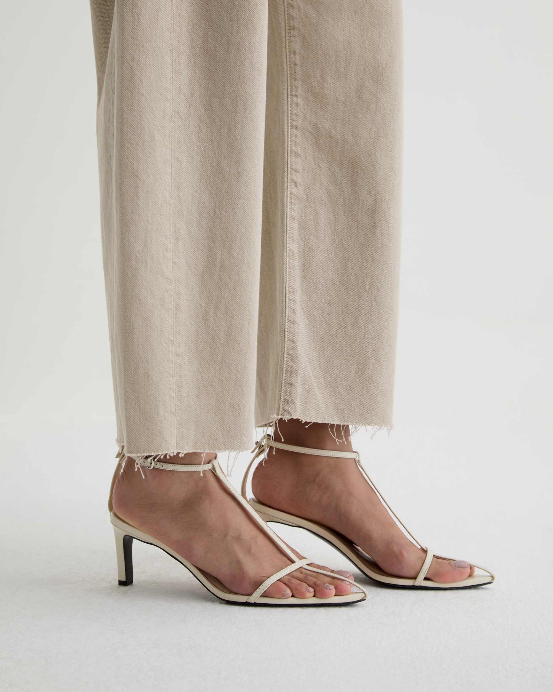 Beige high-heeled sandals worn with light-colored pants on a white background
