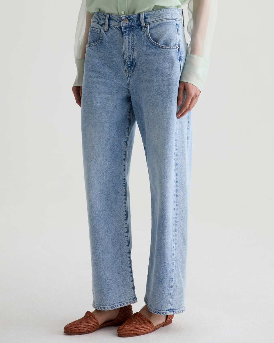 Person wearing light blue jeans and brown shoes on a white background