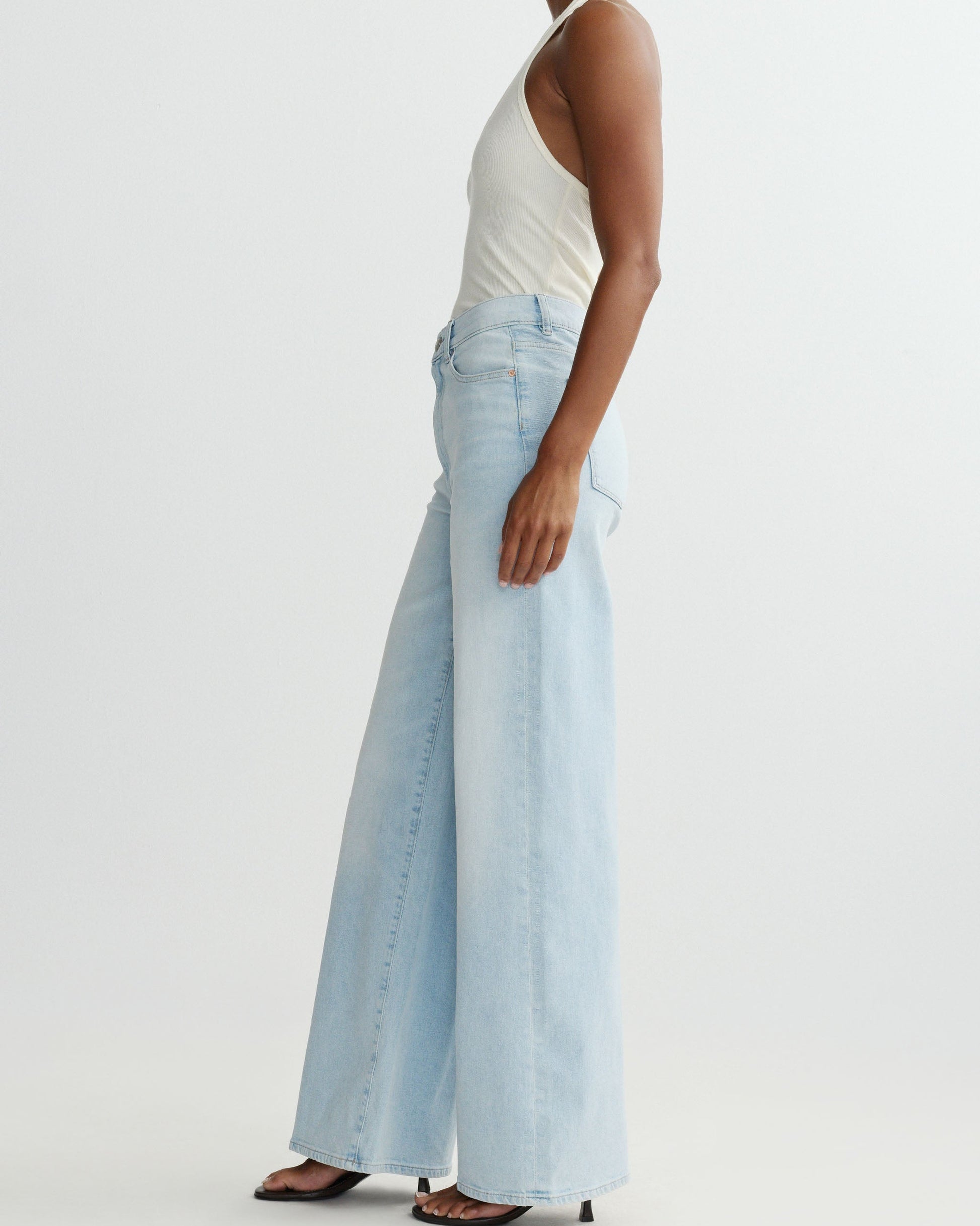 Person wearing light blue jeans and a white top on a plain background