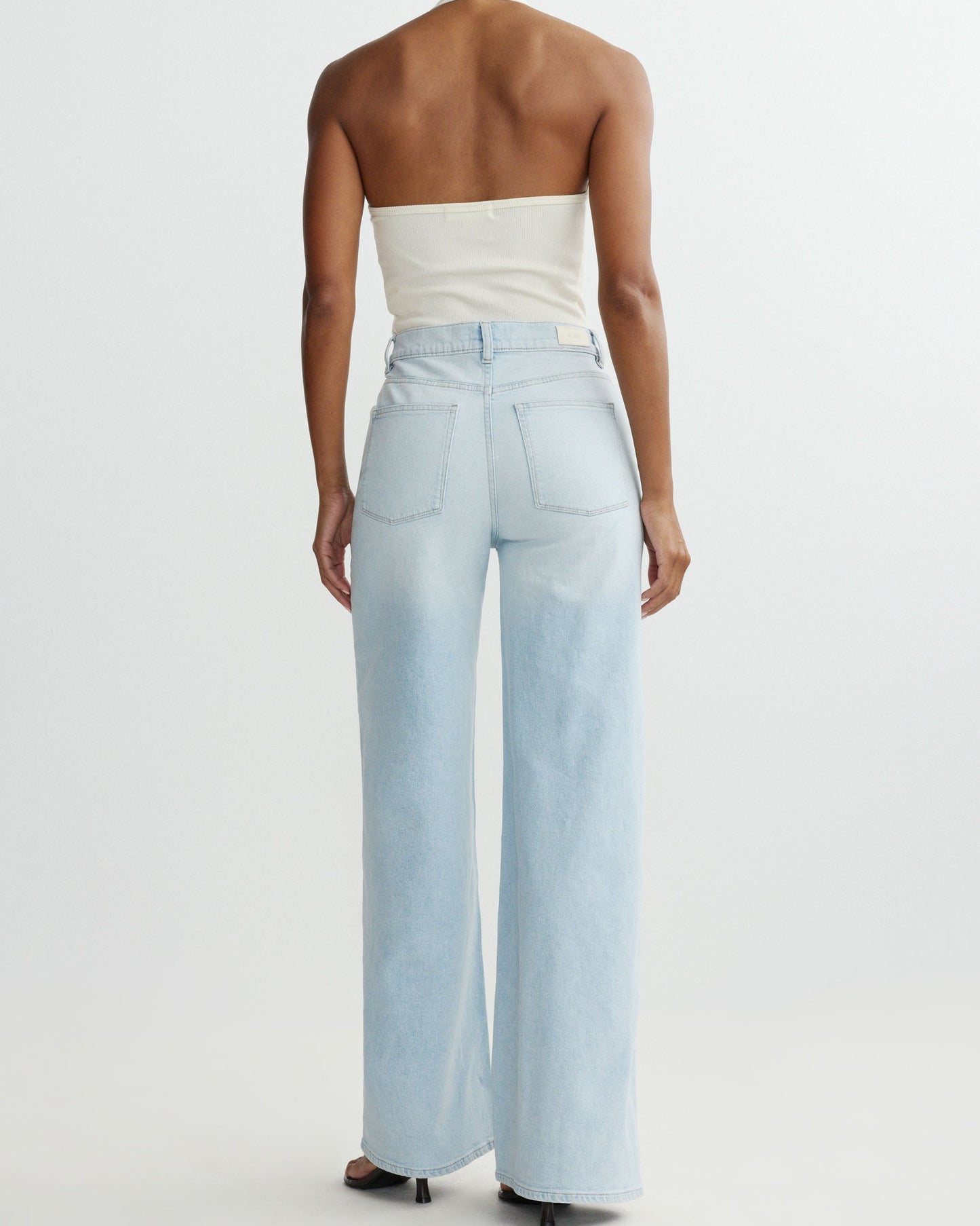 Person wearing light blue wide-leg jeans and a white strapless top on a white background