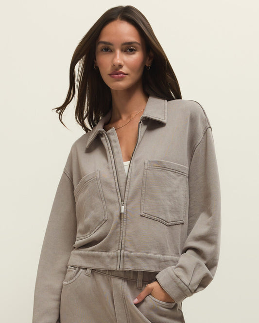 Woman wearing a gray zip-up sweatshirt and pants on a beige background