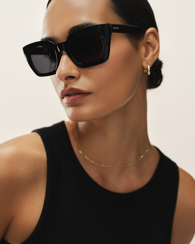 Woman wearing black sunglasses and a black sleeveless top against a light background