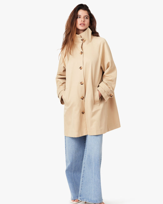 Woman wearing a beige coat and blue jeans on a white background