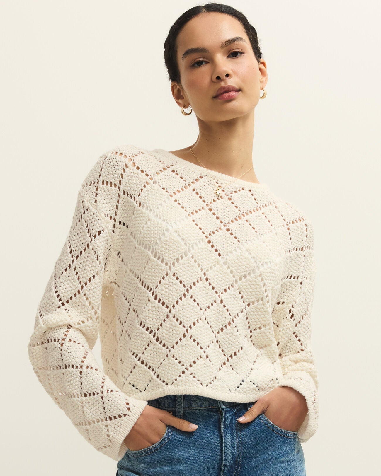 Woman wearing a white lace sweater and blue jeans on a plain background