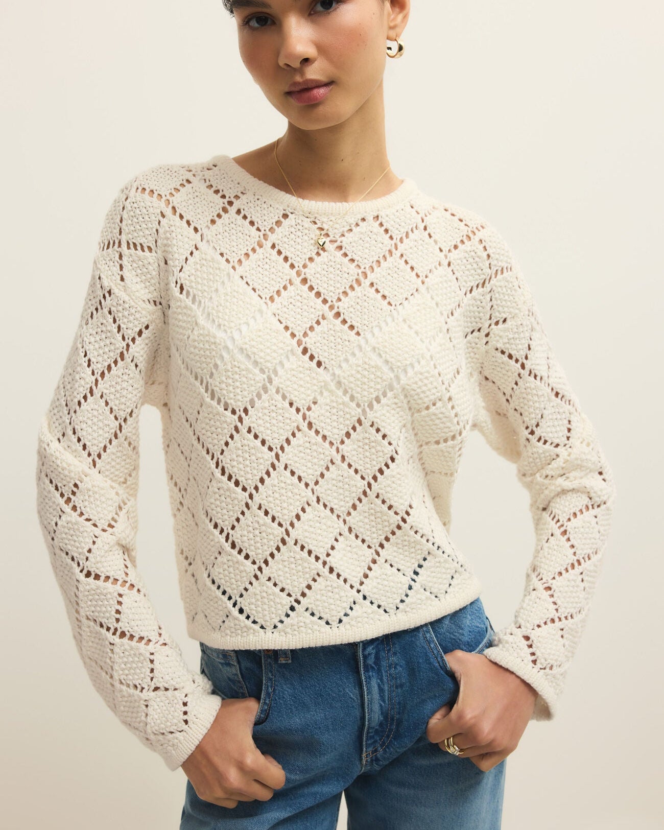 Woman wearing a white textured sweater and blue jeans against a plain background