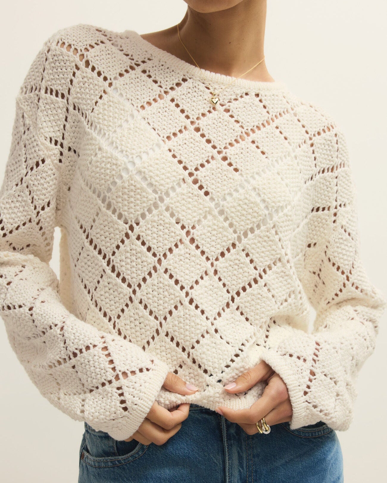 Person wearing a cream-colored knitted sweater and blue jeans against a neutral background