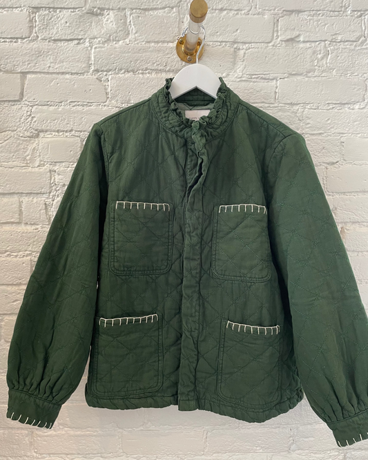 Green jacket on a hanger against a white brick wall