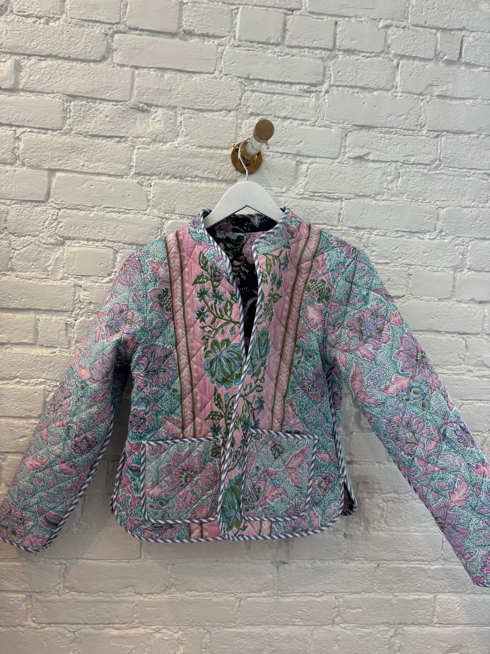 Floral patterned jacket on a hanger against a white brick wall.