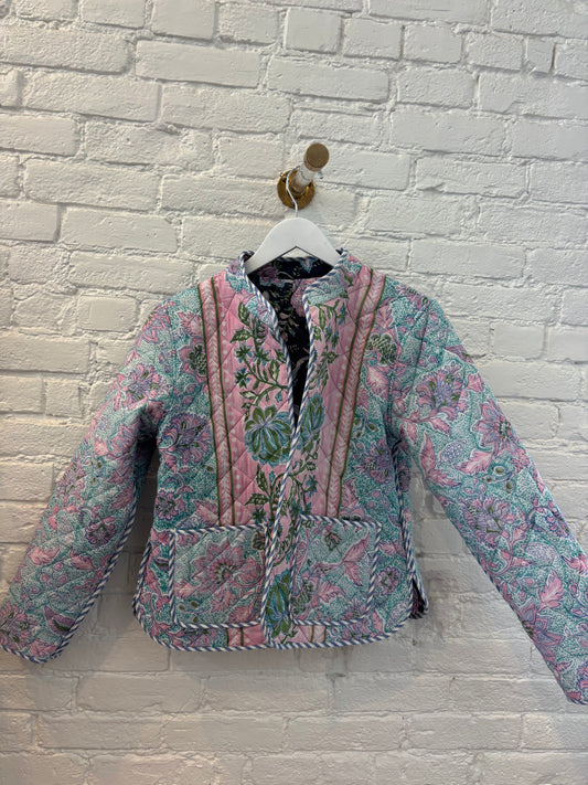 Floral patterned jacket on a hanger against a white brick wall.