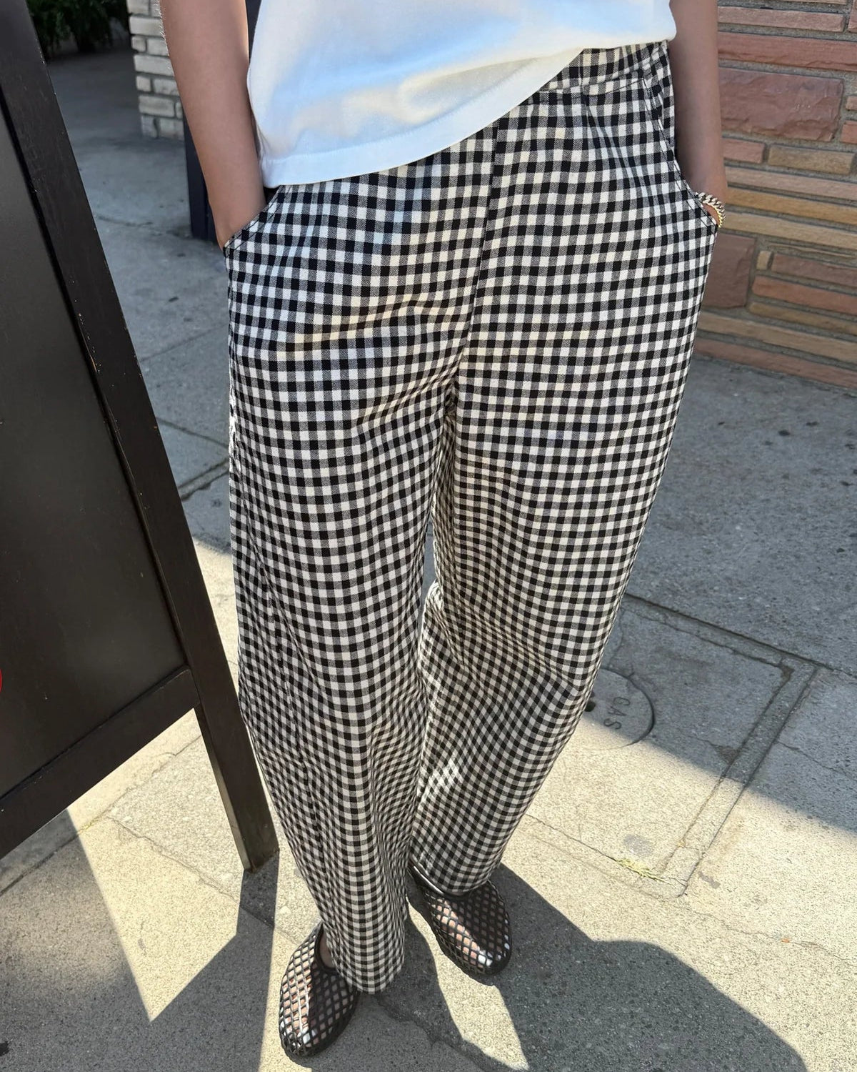 Person wearing a white top and black and white checkered pants on a sidewalk.