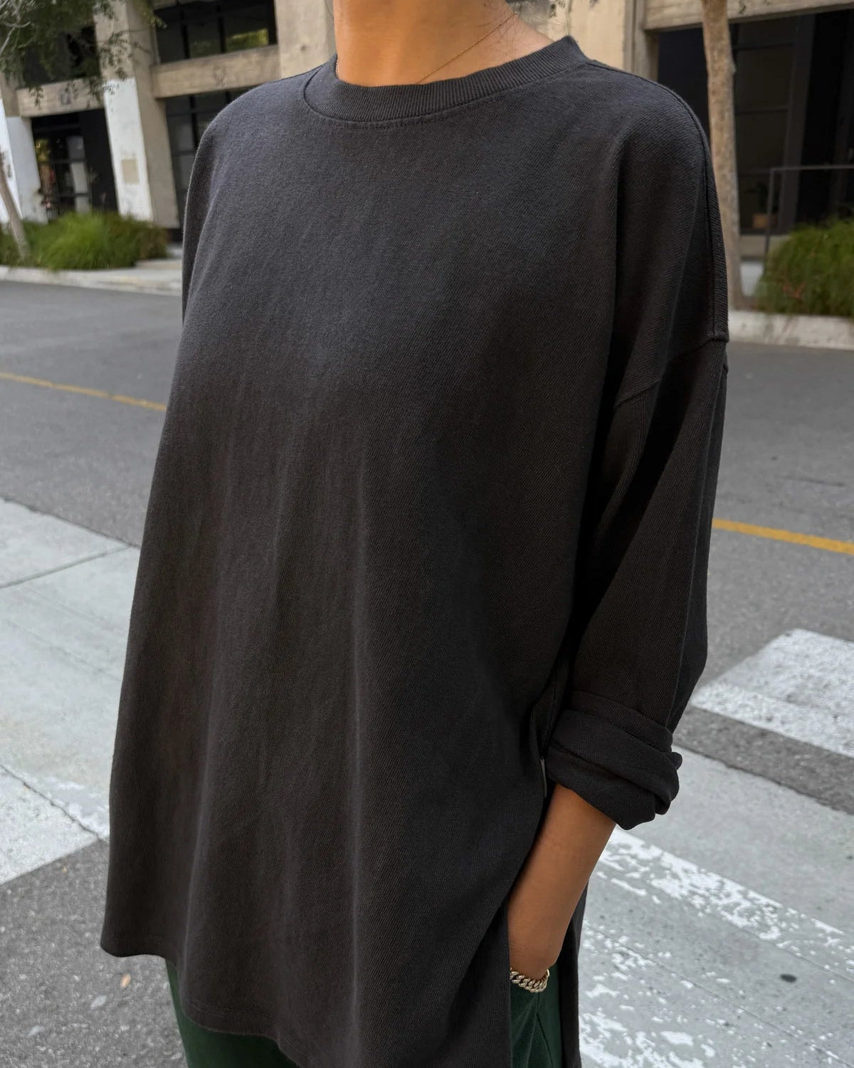 Person wearing a black oversized sweatshirt and green pants on a street.