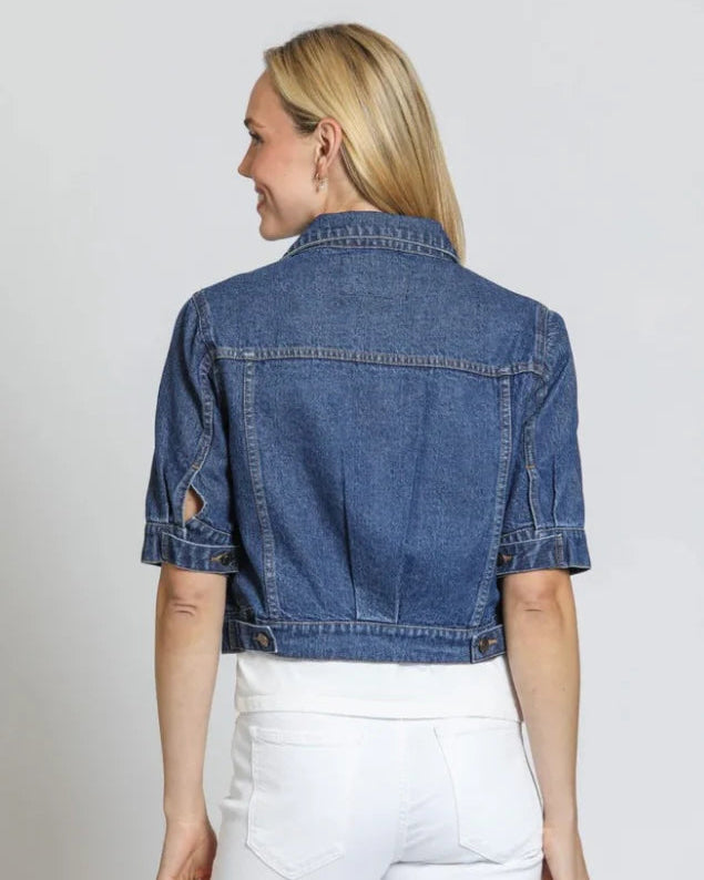 Woman wearing a blue denim jacket and white pants on a plain background