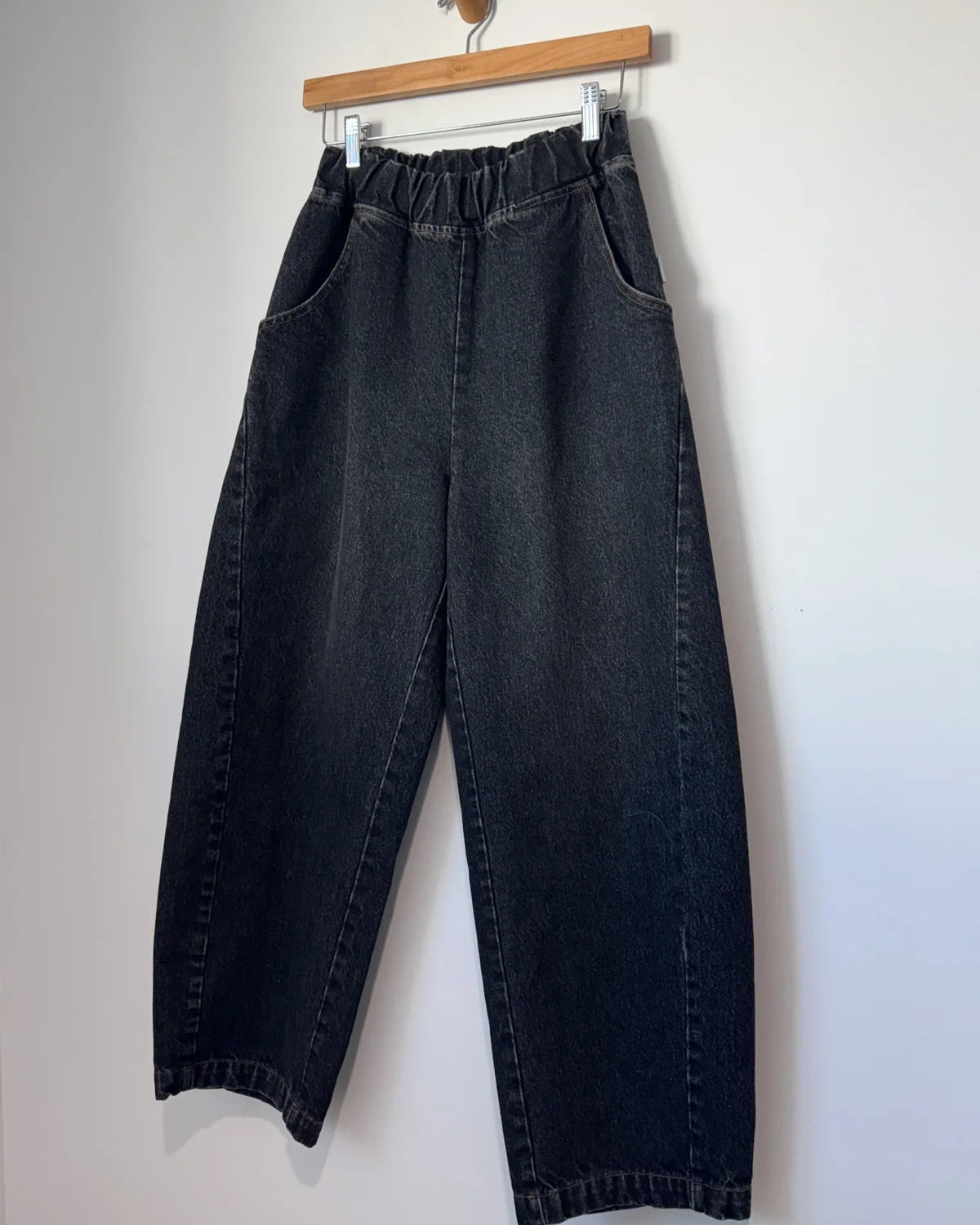 Black jeans hanging on a wooden hanger against a white background