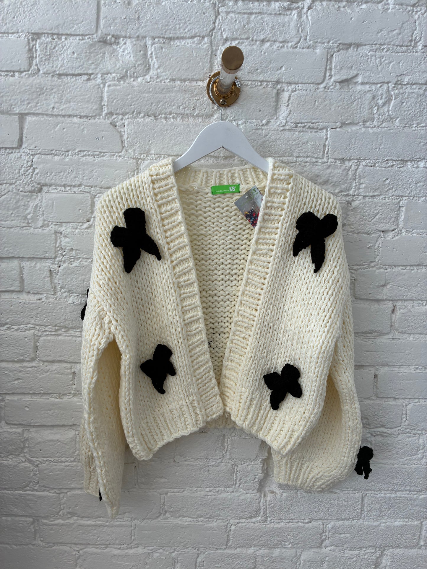 white knit cardigan with black knit bows on white brick background