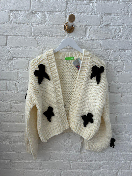 white knit cardigan with black knit bows on white brick background