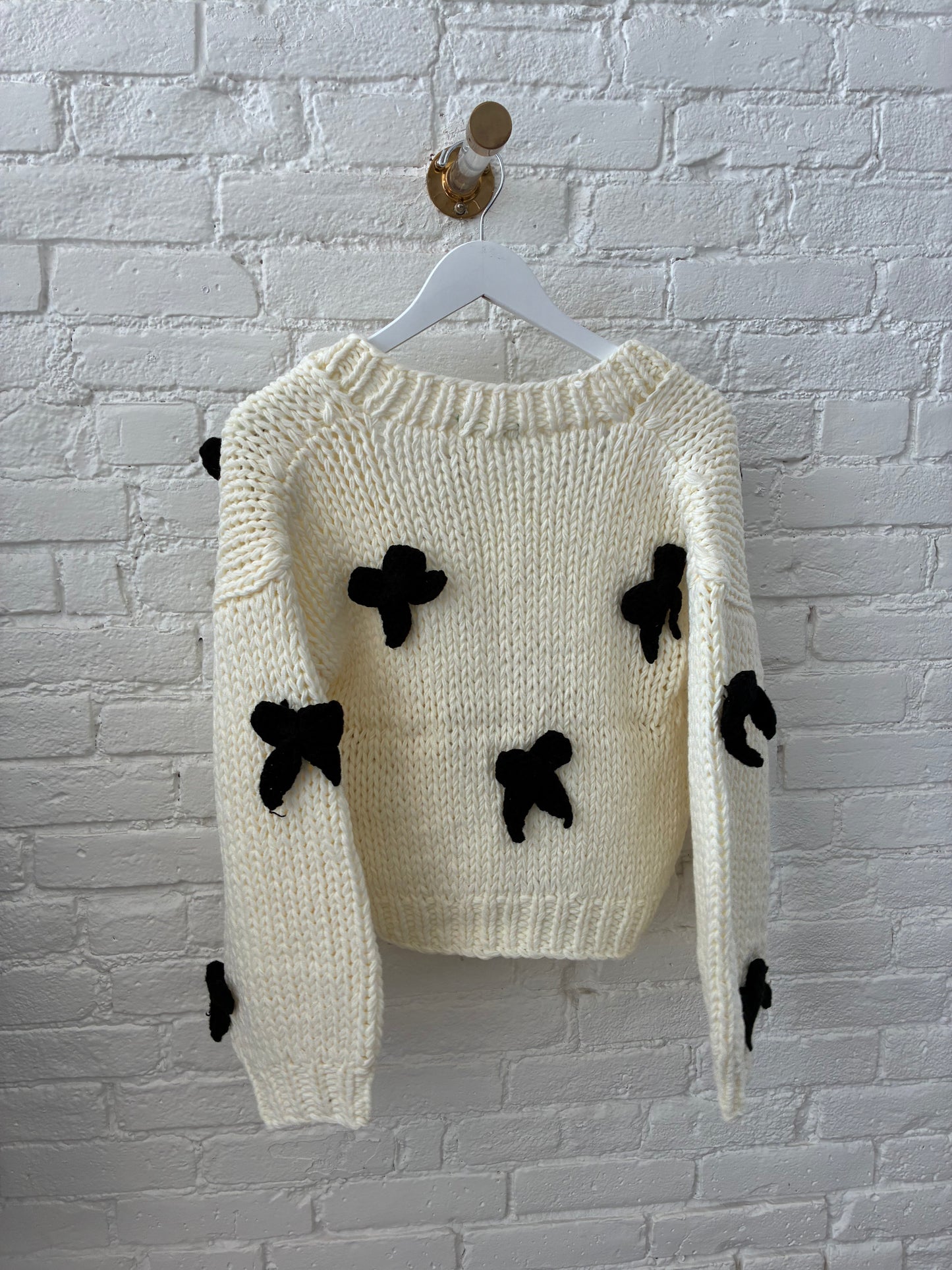 backside of white knit cardigan with black knit bows on white brick background