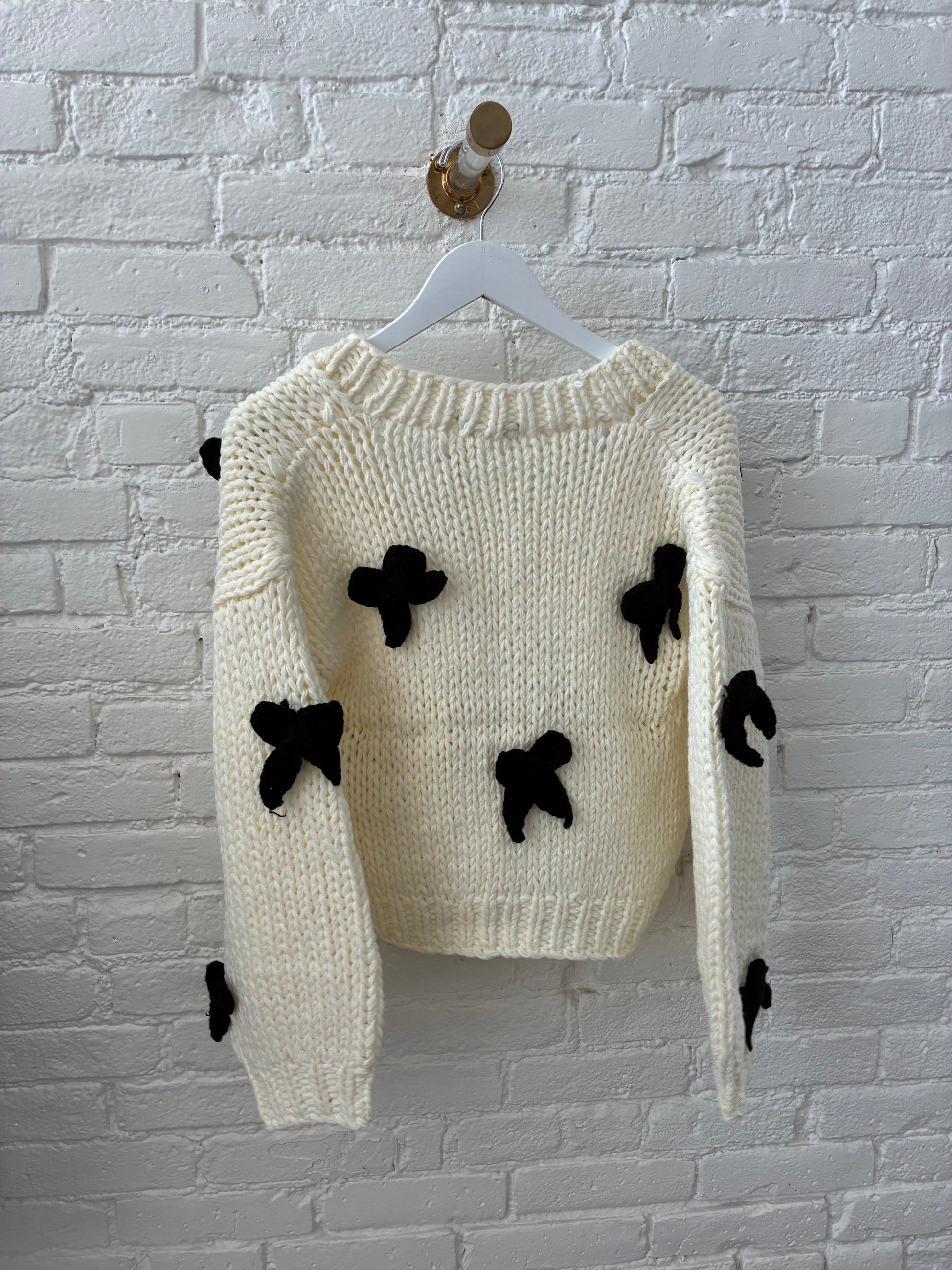 backside of white knit cardigan with black knit bows on white brick background
