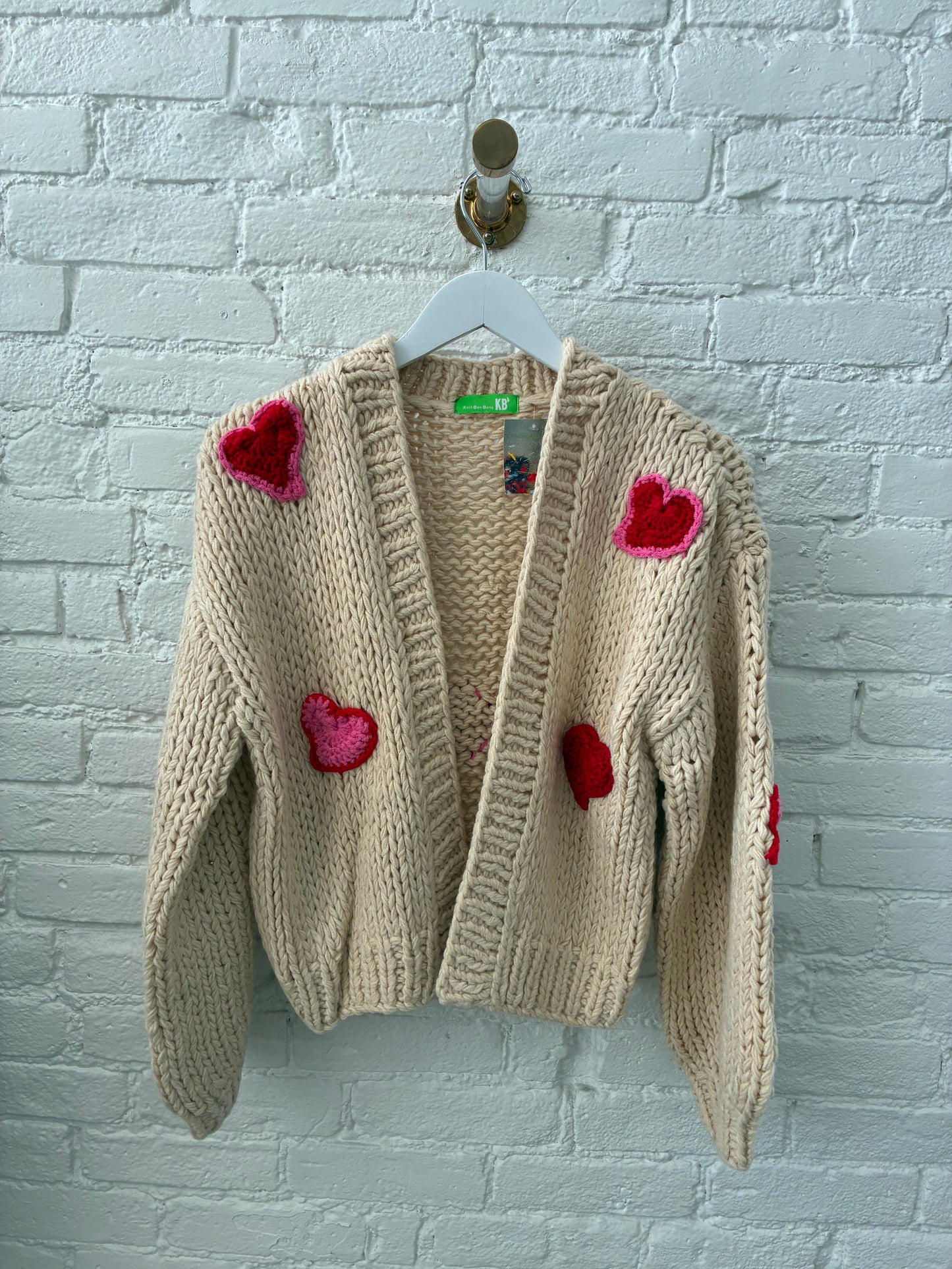 beige knit cardigan with pink and red knit hearts on white, brich background