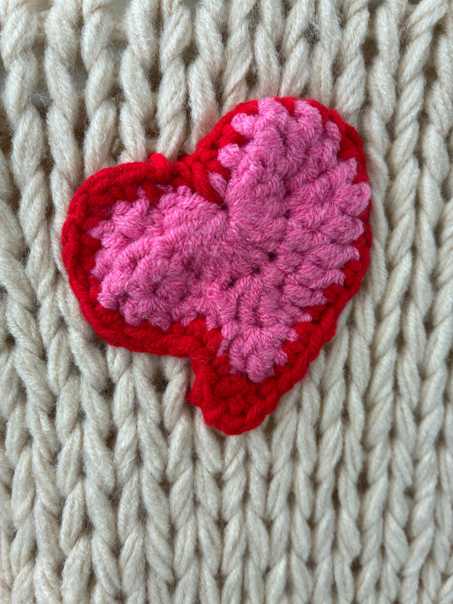 Heart-shaped pink and red crochet patch on a beige knitted fabric background